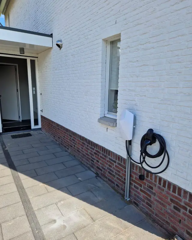 Laadpaal met kabelhouder aan een witte gevel