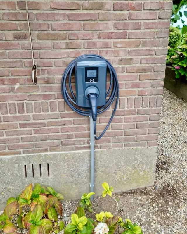Laadpaal met opgerolde kabel aan een bakstenen muur