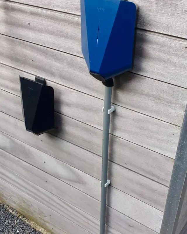 Laadpaal met blauwe cover aan een houten gevel