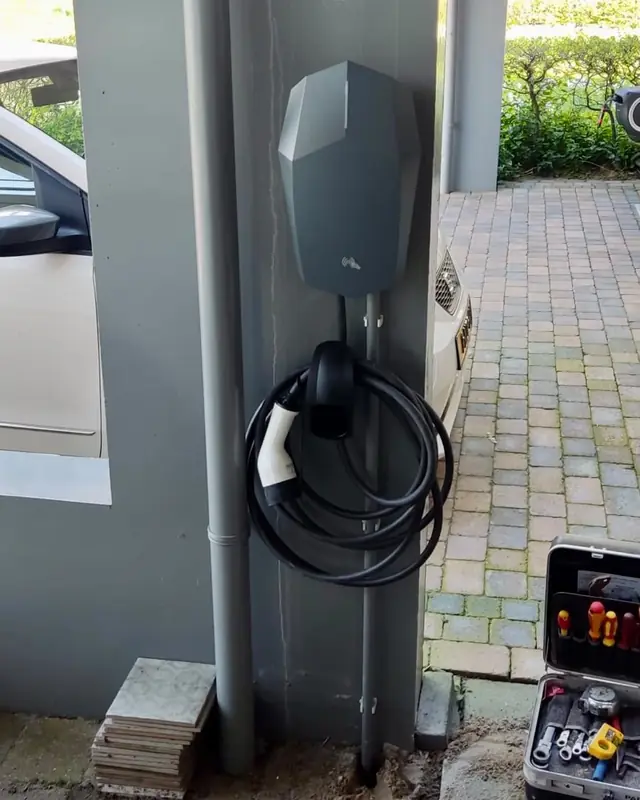 Laadpaal met kabel aan een pilaar bij de carport