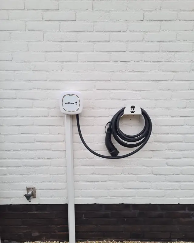 Laadpaal met kabelhouder aan een witte gevel