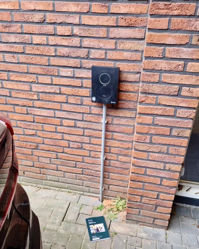 Laadpaal met kabelgoot aan een bakstenen gevel