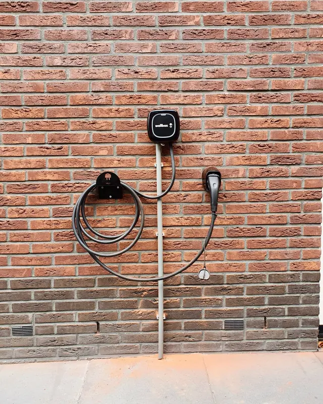 Wallbox-laadpaal met kabelhouder aan een bakstenen muur
