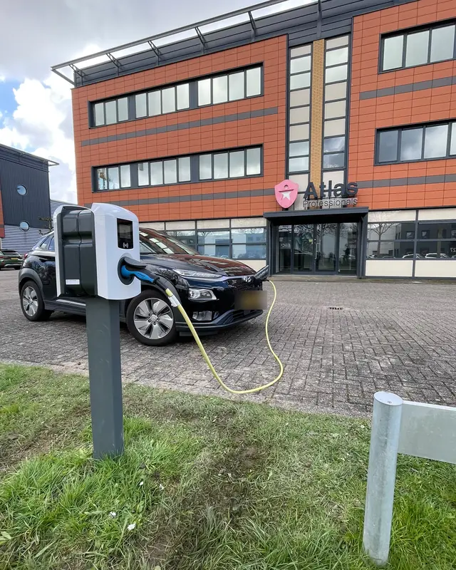 Zakelijke laadpaal bij een kantoorpand, met een ladende auto