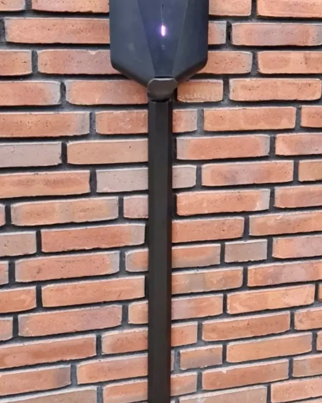 Laadpaal met kabelgoot aan een rode bakstenen muur