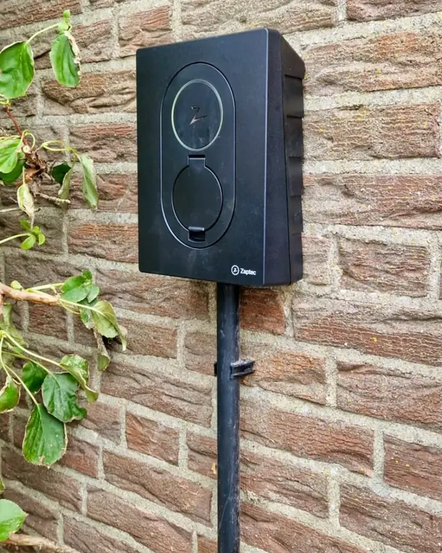 Laadpaal aan een bakstenen muur met klimop