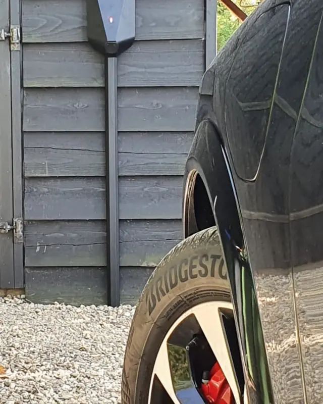 Laadpaal aan een houten schuur bij de oprit