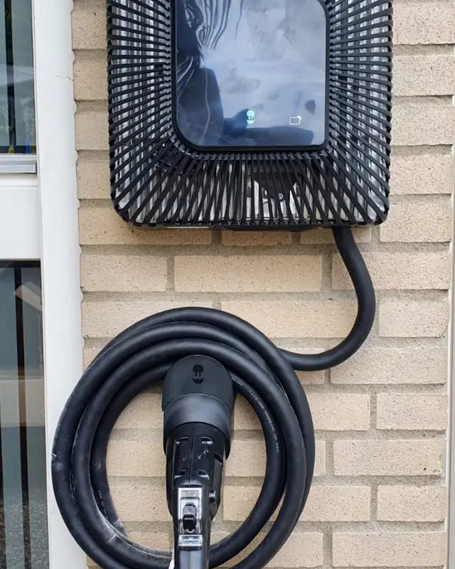 Laadpaal met opgerolde kabel naast een raam