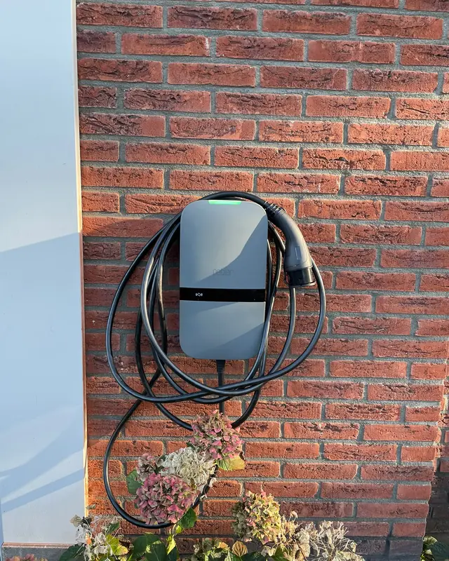 Laadpaal met opgerolde kabel aan een bakstenen gevel